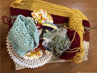 Yarn skeins and multiple knitting and crochet projects including a mustard and burgundy scarf or shawl, light blue crocheted piece, and flower-like motifs.