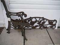 Two cast iron bench end frames and one decorative back panel leaning against a wall