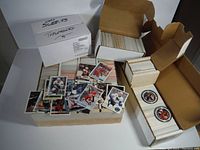 Boxes filled with roughly 6000 hockey cards, with a loose pile of cards displaying various players on top, and boxes labeled with sleeves and top loaders.