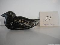Side view of a black soapstone seabird carving, showing outline and carved wing detail with card labeled 57.