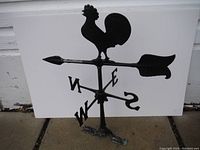 Full view of black cast aluminum weather vane with rooster figure on top and directional letters N, S, E, W. White background showing the entire piece and its height.