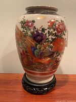 Front view of Asian vase showing intricate floral and bird paintings and crackled finish on ceramic surface, sitting on wood stand.