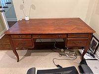 Front view of wooden desk showing veneer top, cabriole legs, three top drawers and two bottom file drawers