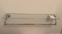 Front view of the rectangular glass shelf mounted on the wall with chrome supports and towel bar below, showing overall condition and dimensions.