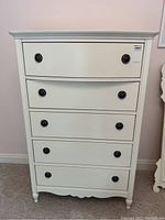 Front view of white chest showing five drawers and hardware