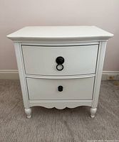Front view showing two drawers, decorative handles, curved legs, and scalloped bottom trim.