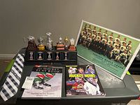 Photo showing overall hockey collectibles including replica trophies, books, framed photo and necktie.