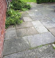 View of laid limestone patio stones against brick wall with adjacent garden bed