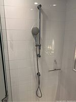 Full view of shower head mounted on white tiled wall with adjustable slide bar and flexible hose hanging down.