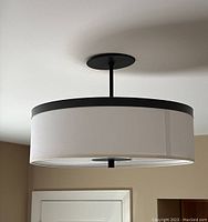 Side view of modern ceiling light mounted on ceiling, showing white fabric drum shade and black metal trim and mount.