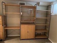 Full view of the entire modern shelving unit showing three sections: two open shelving units with wooden shelves and metal frames flanking a central wooden cabinet with glass doors.