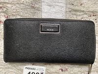 Front view of Tumi black leather wallet with textured surface and front logo plate.