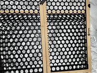 Close-up image showing wooden frame and black mesh panel with circular holes of the safety gate.
