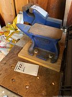Photo of small blue anvil and larger anvil in background on wooden workbench surface with label reading '722 Anvil'.