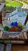 Crystal bowl containing several glass grape clusters on a wooden shelf with outdoor seating in background.