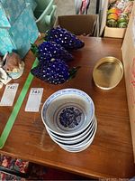 Photo showing eight stacked blue and white porcelain bowls with dragon designs inside, alongside three blue crystal berries with green stems, all displayed on a wooden surface.