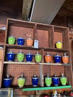Photo of wooden shelf with 17 ceramic candle containers of different colors and metal lids arranged on it