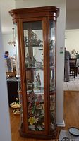 Front view of wood framed display cabinet filled with figurines, showing interior glass shelves and lighting.