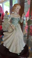 Front and left side view of Royal Doulton porcelain figurine of a woman in a white gown with a pale blue bodice, holding a flower.