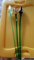 Three hand blown glass flowers on a yellow surface, showing full length of long green stems and flower tops.