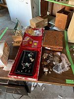 Overview of jewelry on table including decorated fabric boxes, assorted jewelry pieces spread on table, and a central red box lined with black velvet.
