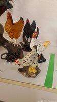 Four rooster and chicken figurines on display, showing variety and detailed molding.