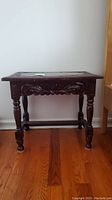 Front view of the carved wooden side table showing intricate detailing on the apron and turned legs.