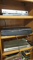 DVD players and turntables arranged on wooden shelves, showing the front of equipment including buttons, inputs, and dust covers.