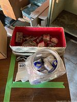 Overview photo showing a white woven basket with red fabric lining filled with various decorative pieces and nearby glass bowl filled with small plastic containers holding thimbles