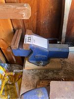 Side view of the blue metal bench vise with wooden jaw inserts and attached wooden base showing wear and rust spots.