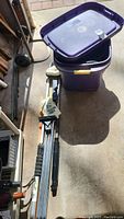 Overall view including purple plastic lidded bin with lid beside it, electric cords coiled near it, and black and silver car washer components.