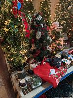 Photo showing multiple illuminated faux trees, greenery with berries, ceramic snowmen on table, candles, and XL red sweatshirt with Christmas decorations on the table.