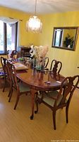Dining table and six matching chairs in a dining room setting with yellow walls and light wood floor.