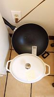 White Palm brand Dutch oven with lid and note on top, black T-Fal non-stick wok below.