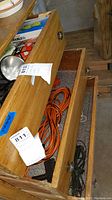 Photo of wooden drawers containing orange extension cord, black electrical cord, and boxed lightbulbs