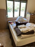 Full view of full size bed frame and headboard with mattress and piled bedding on top by window.