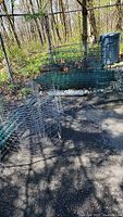 Photo showing multiple rolls of wire fencing coiled and laid on the ground near a chain-link fence outdoors.