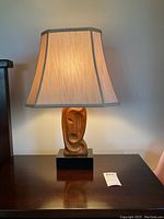 Full front view of illuminated lamp showing carved wood base and beige shade with black trim