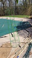 Green wire tomato cages standing on concrete near garden pool.