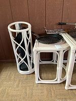 Photo showing the white rattan umbrella stand with visible wear and two of the nesting tables partially visible with some items on top.