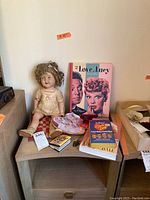 Photo showing Shirley Temple doll, For the Love of Lucy book, heart-shaped plate, and several books on a small table
