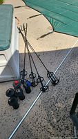 Five metal tiki torches laid on ground next to coolers and covered pool, showing torch holders and pointed ends.