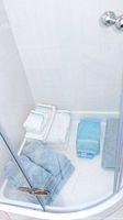 Glass-enclosed shower base with folded white bath towels, hand towel, and light blue bath mat.