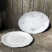 Two antique platters displayed outdoors on wooden surface showing size difference and general condition.
