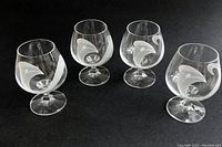 Four clear crystal brandy snifter glasses with white calla lily design on black background, showing curved bowl and ribbed foot.
