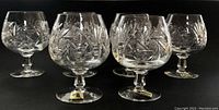 Front and side view of six heavy crystal brandy glasses showing clear intricate cut pinwheel hobstar and fan patterns. One glass has visible thinner rim.
