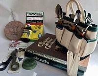 Gardening tote with tools, plant markers, bottles of Superthrive solution, metal frog flower arranger, gardening books, and garden face plate shown for overall lot content.