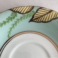 Close-up of saucer showing hand-painted leaves and foliage detail with gold trim on mint green background.
