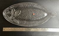 Top-down view of the entire fish-shaped glass platter with a ruler underneath showing about 19 inch length.