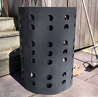 Perforated vinyl sheet formed into a barrel shape with circular holes, black color, outdoors on patio.